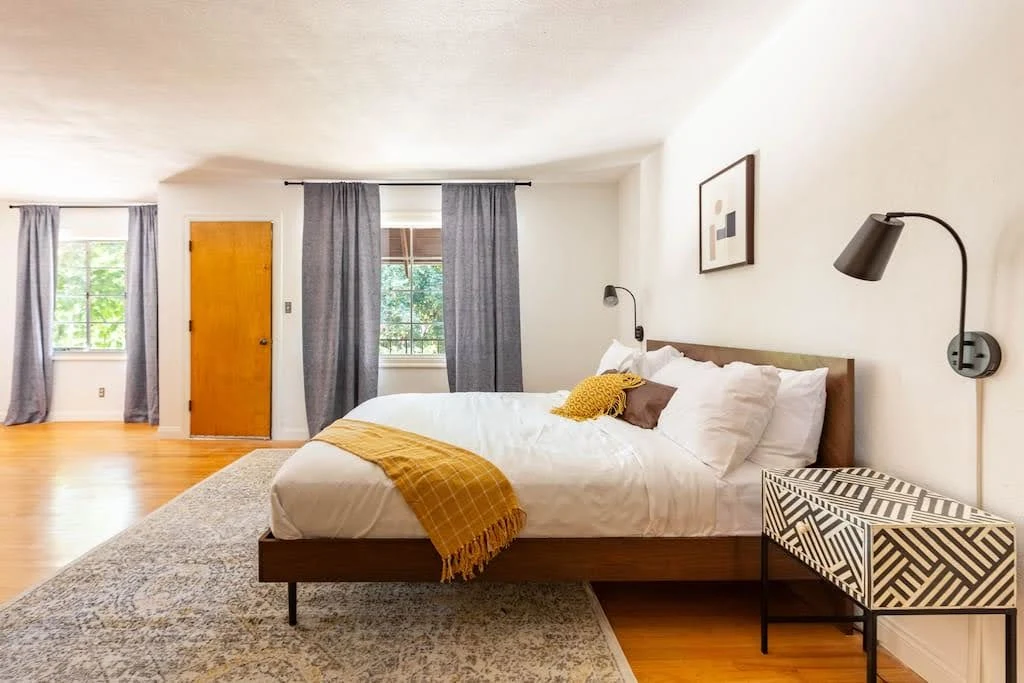 Airbnb bedroom with mustard bedding, a woven bench, wall lamps, and warm wood accents