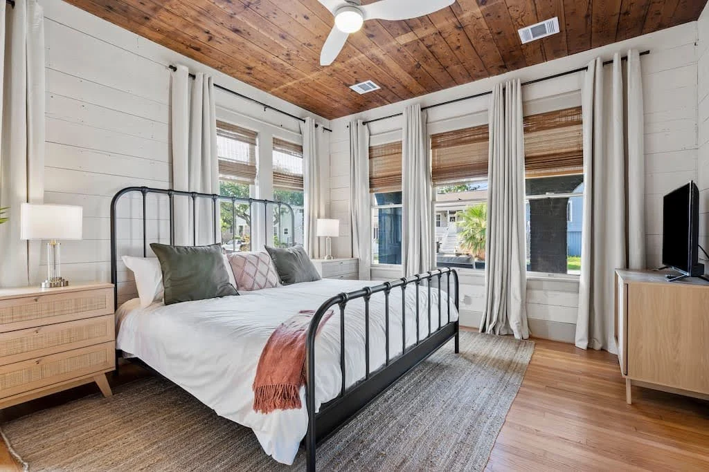 Airbnb bedroom with exposed brick, tall windows, and a black metal bed