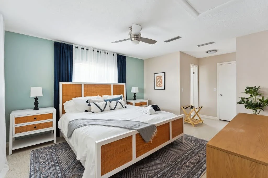 Airbnb bedroom with sage walls, warm wood furniture, and patterned white bedding
