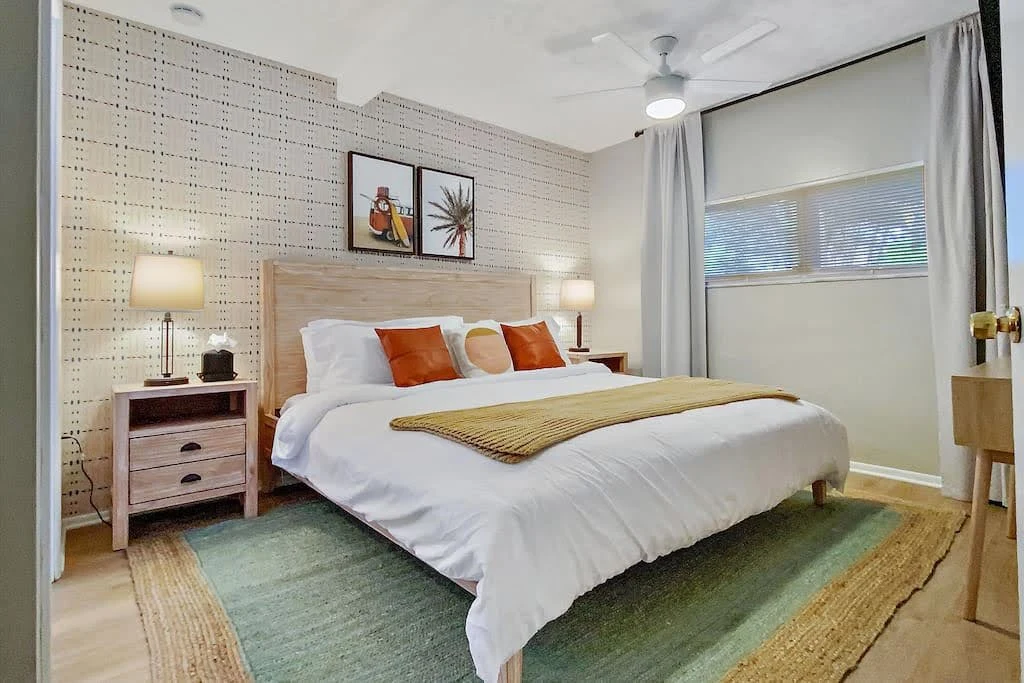 Airbnb bedroom with green and orange accents, wood furniture, and large windows